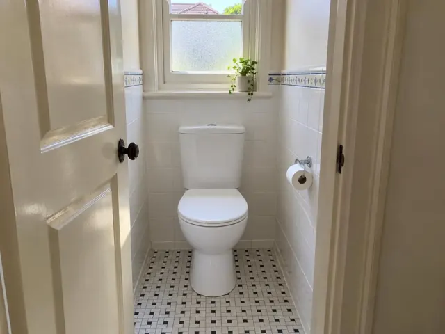 Clean white toilet in a tiled bathroom with a window and door in Kogarah
