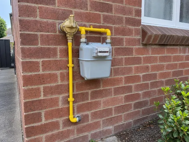 Outdoor gas meter and yellow pipework on a brick house wall beside a window in Rockdale