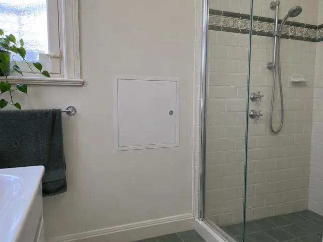 Bathroom wall with small access panel beside a tiled shower and vanity in Bexley